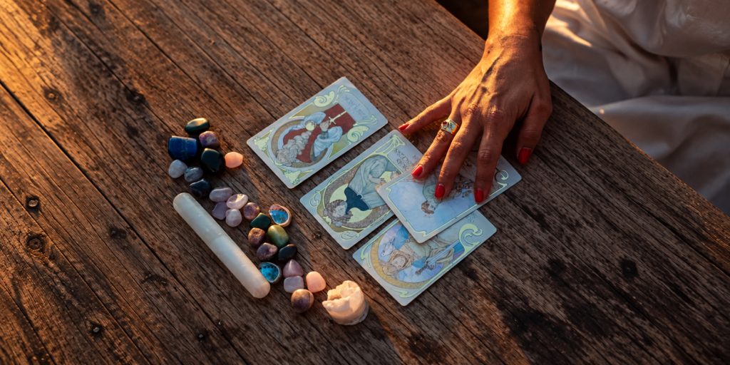 Mano de Clara sobre cartas de Tarot, piedras y una vela en una mesa de madera.